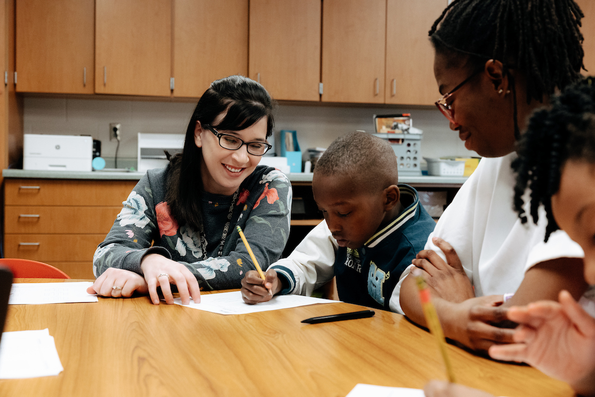 Mentor teacher in elementary classroom with student teacher and student at table